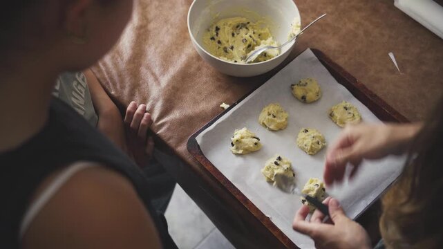 Mother baking cookies at home with her daughters watching the process, focusing on the tactile process of homemade baking and warm family interaction concept
