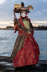 Obraz premium Venice, Italy - February 09, 2026: Elegant masked figure in elaborate costume holds a pistol at Venice Carnival, with water and skyline visible in the background