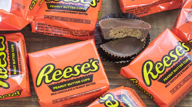 NORWALK, CT, USA - FEBRUARY 24, 2026:Several Reese's peanut butter cups are on a wooden table. Some wrappers are crumpled up around the treats. One cup is cut in half showing the creamy inside.