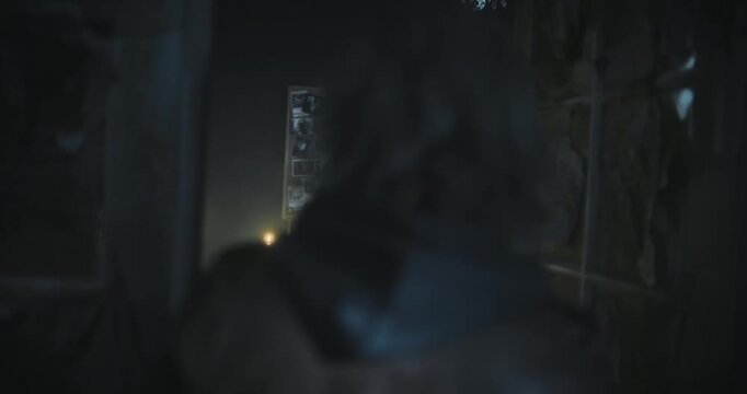 Handheld shot following behind young woman as she enters spooky room with candlelight