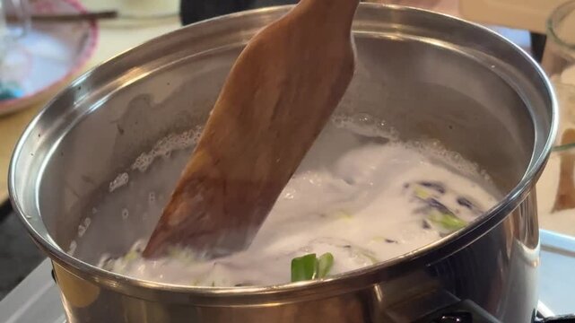 Stirring a Pot of Coconut Milk with Butterfly Pea Flowers to Make Thai Sticky Rice with Mango