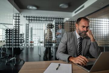 Stressed businessman working on laptop in modern corporate office