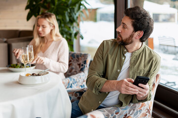 Man secretly texting on smartphone, ignoring woman during restaurant date