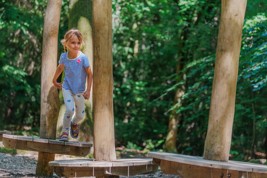 Cute running girl playing on wooden balance beams in forest park