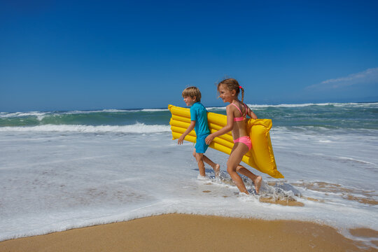 Happy kids children playing in waves with inflatable mattress