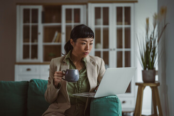 Asian woman working remotely with laptop and coffee