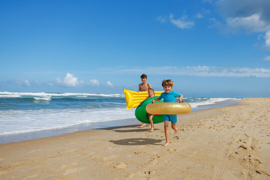 Group of happy kids running on beach with inflatable floaties