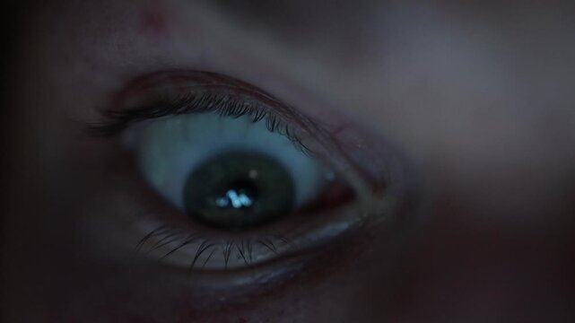 Close up of tired eye illuminated by screen light anxious gaze following falling cryptocurrency market reflected in pupil dramatic tension and financial uncertainty at night