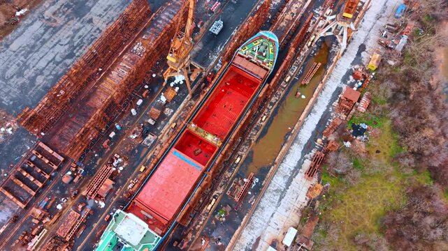 Top down view of cargo ship in shipyard dry dock. A red cargo ship hull undergoing repairs in a shipyard dry dock facility.