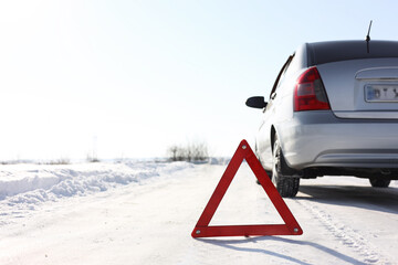 Warning triangle and broken car on roadside at snowy winter. Space for text