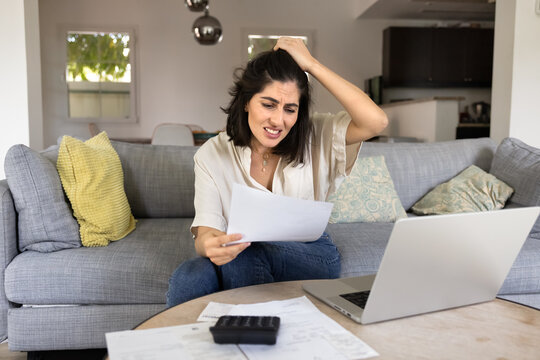Frustrated worried young Latin woman counting too high expenses, reviewing bill, invoice for payment, touching head, feeling regret, despair about financial loss, reading paper letter