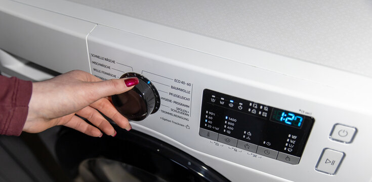 Woman hand choosing program on automatic washing machine for laundry at home. Turning knob on control panel