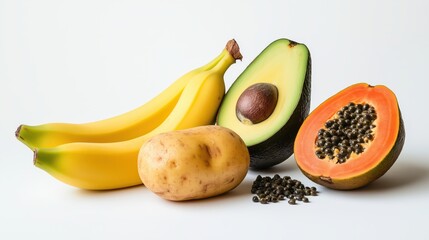 A unique and diverse collection of fresh produce is arranged on a clean white background, featuring ripe yellow bananas, a halved green avocado, a sliced orange papaya, and a single brown potato.