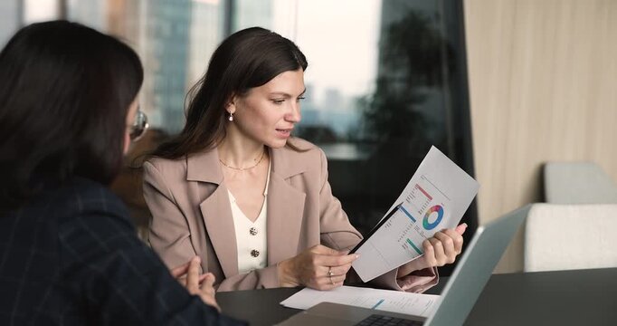 Businesswoman analyzing printed financial charts, review performance metrics, discussing business report with colleague at laptop during corporate office meeting. Consulting, budget, market research