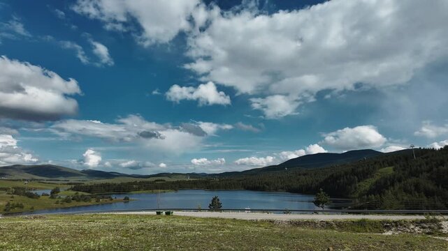 Timelapse of Ribnicko jezero with cable car line moving above calm water and rolling mountain hills under dramatic blue sky. Scenic nature landscape and travel destination in Zlatibor region