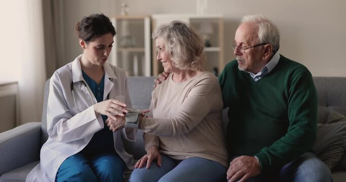 Nurse assists to senior woman with home blood pressure check, placing and adjusting cuff on her wrist for monitoring heart and vascular health, control hypertension during home visit to retired couple