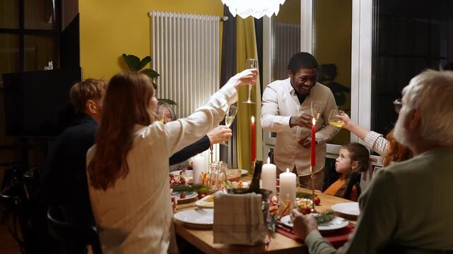 Male guest stands and clinks glasses with family and guests sitting at table