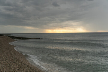 Pebble beach, Black Sea coastline under dramatic cloudy sky with soft light near horizon, wide coastal perspective, muted gray blue tones. Image supports tourism, wellness communication