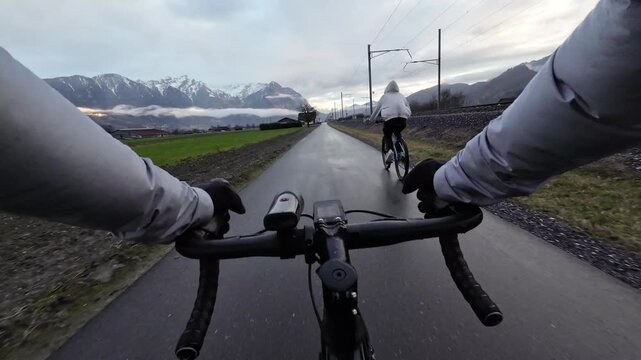 POV shot of cyclist overtaking another cyclist on narrow rural road with railway nearby, active commuting and mobility concept