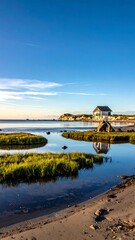 Naklejka premium Serene beach with calm water reflecting a house under a clear blue sky at sunset