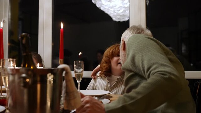 Grandfather hugging and talking to his grandson while they sit at the table