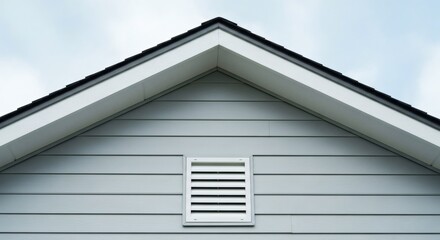 Modern residential building exterior featuring a clean architectural gable peak and a functional white vent against a bright sky