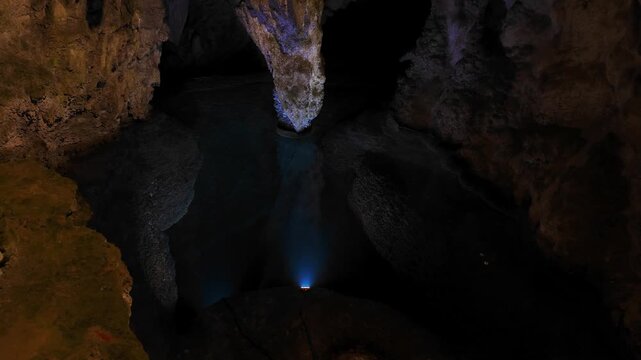Underground chamber of Stopica Cave in Zlatibor with dramatic lighting reflecting on dark water surface. Natural limestone formations create a mysterious atmosphere inside the Serbian cave