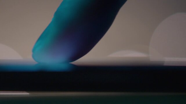 Scrolling Social Media Posts on Smartphone in Dark Ambience. Extreme closeup view of male finger scrolling up and down on the screen of a smartphone at night time. Shooting in slow motion. Selective f