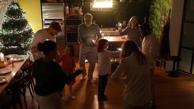 Grandson talking to male guest while family with guests dances and holds sparklers around them
