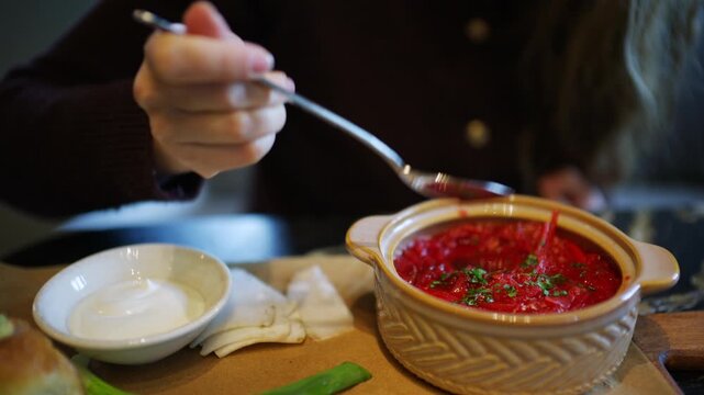 Close up of a hand holding a spoon above a bowl of borscht garnished with herbs