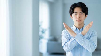 胸の前で腕を交差させダメというサインを出す若い男性 ｜ ボケみ背景