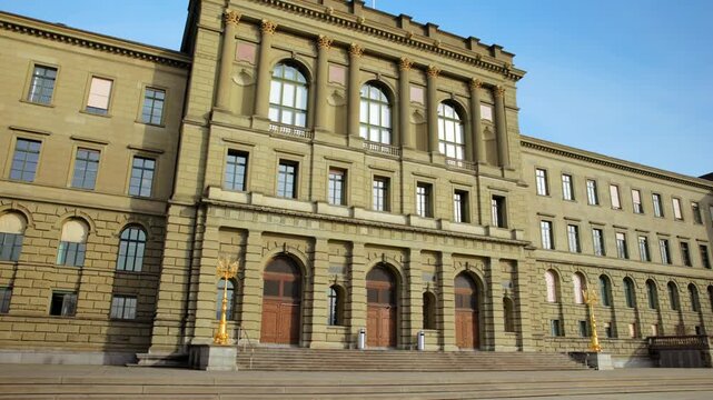 Panning shot of the majestic main building of ETH Zurich, showcasing its grand neoclassical architecture, stone facade, and ornate details under a bright blue sky in Switzerland.