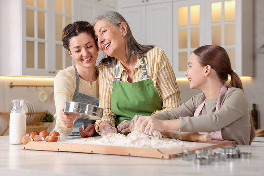 Smiling grandmother, her daughter and granddaughter cooking together at white marble table in kitchen