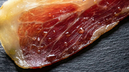 Macro of paper-thin slice of aged Jamon Iberico with translucent sweating fat