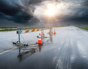 Flooded road with construction barrier and cones during storm and dramatic light