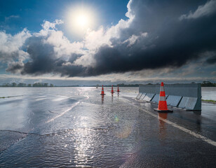 Flooded road with construction barrier and cones during storm and dramatic light