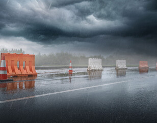 Flooded road with construction barrier and cones during storm and dramatic light