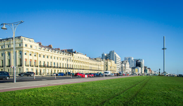 Street view of Brighton beach front buildings in a sunny day with green grass and blue sky.