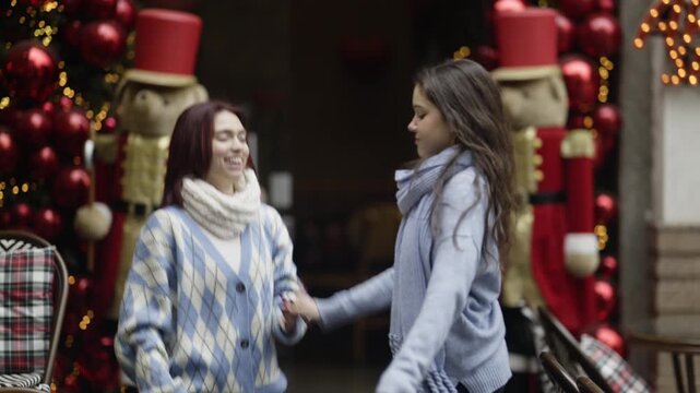Cheerful young friends dance playfully together in a festive winter setting. They enjoy a happy moment amidst holiday decorations.