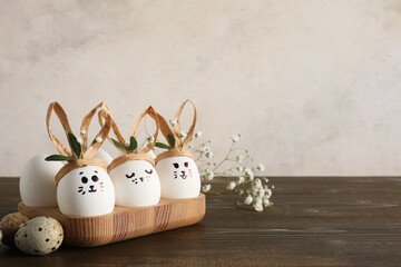 Naklejka premium Tray with creative Easter eggs, leaves and flowers on brown wooden table near grunge white wall