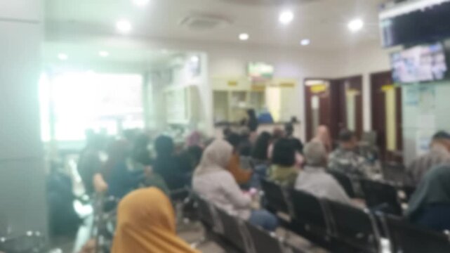 A blurred view of diverse group people are seated in a hospital waiting room, patiently awaiting their turn. The scene captures a sense of anticipation and the common experience of healthcare environm