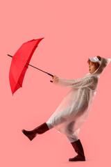 Obraz premium Young woman in white raincoat with umbrella and strong wind on pink background