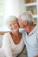 Lovely couple romantic moment. An older couple embracing and sharing a tender kiss on a couch. The man leans in to kiss the woman on the cheek, and they both have smiles on their faces.