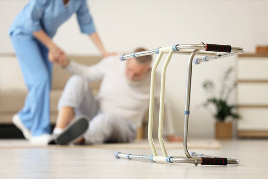 Walker against nurse helping senior man to stand up after fall at home, closeup