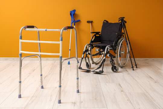 Medical walker with crutches and wheelchair near orange wall