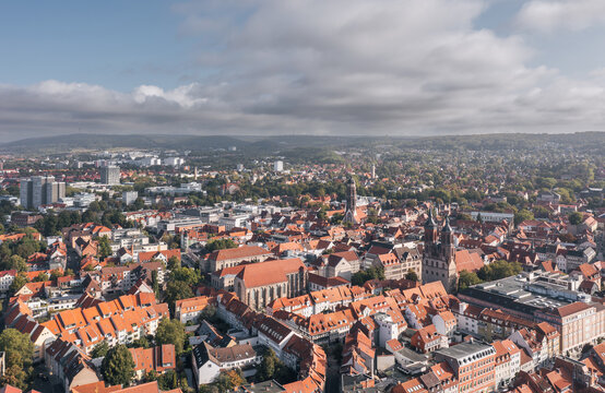 Elevated drone view over the historic old town of Goettingen (G&ouml;ttingen), Lower Saxony, Germany, featuring dense red rooftops, prominent church towers, and a broad city skyline beneath soft clouds.