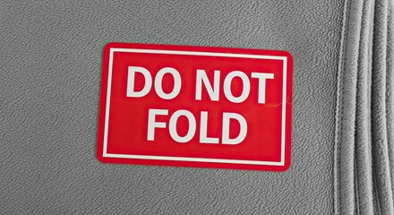 Red 'do not fold' warning sticker on gray textured surface with soft diffused lighting and a vertical crease