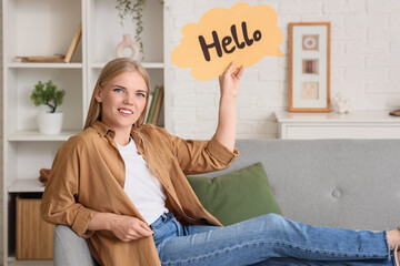 Young woman holding speech bubble with word HELLO on sofa at home © Pixel-Shot