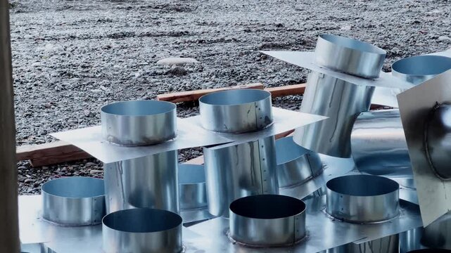 Close up view of stacked galvanized ventilation ducts and round metal fittings at construction site. Detailed shot of HVAC components prepared for installation. Infrastructure concept.