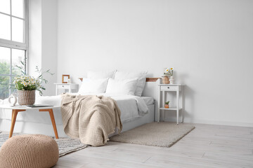 Interior of light bedroom with tables and chamomiles in vases